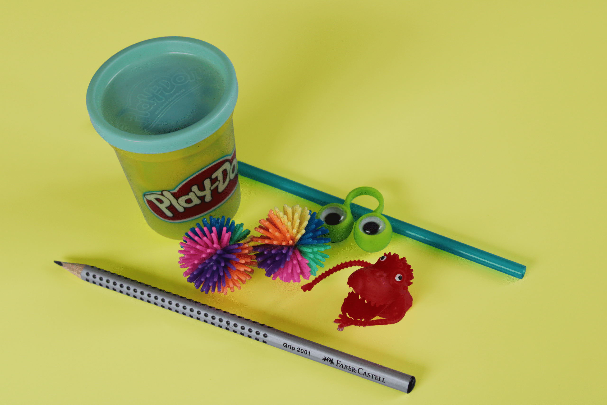 Exemple de petits matériel utilisé en séance pour travailler la motricité des doigts. De la pâte à modeler, des balles à picots, un monstre de doigts, une paille, un finger-eyes et un crayon à papier Faber Castell