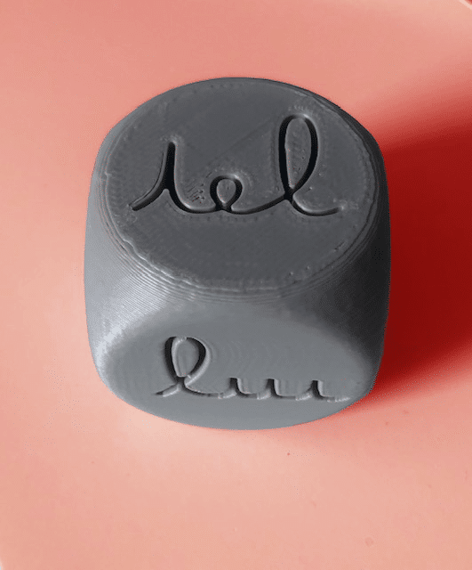 Un dé à jouer gris fabriqué grâce à une imprimante 3D, sur lequel sont tracées différentes petites et grandes boucles et différentes petites et grandes étrécies, utilisé en séance pour travailler le geste d'écriture.